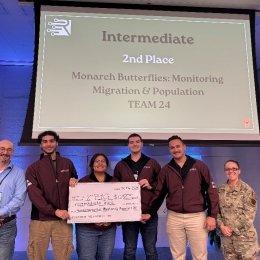 Norwich team at Rowdy Datathon holding their 2nd place prize in front of a sign that says "Intermediate 2nd Place - Monarch Butterflies: Monitoring Migration & Population (Team 24)"