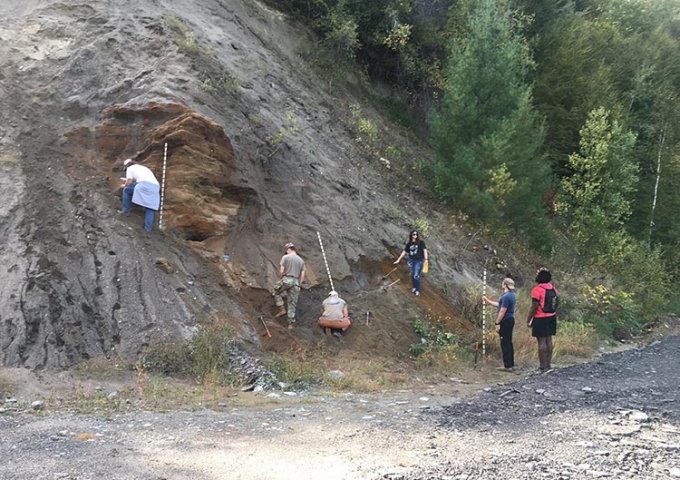 Geology students studying sediment next to a large hillside.