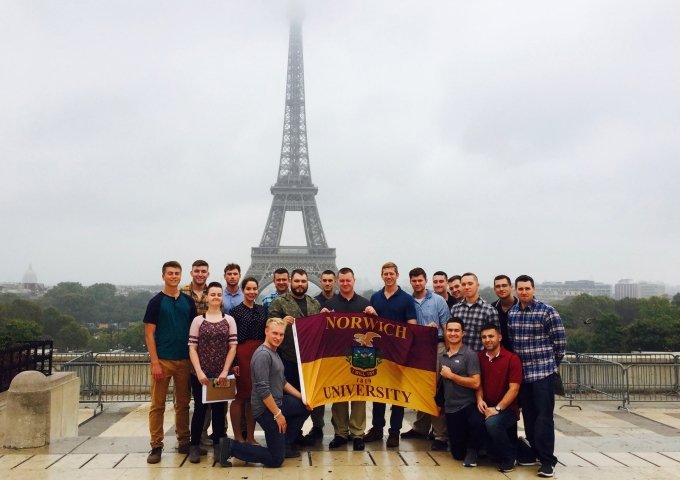 Image of students holding Norwich flag in front of the Eiffel Tower.