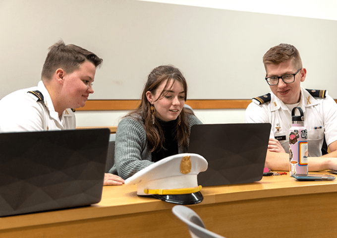 Three students working together on their laptops. Two are in the Corps and one civilian.