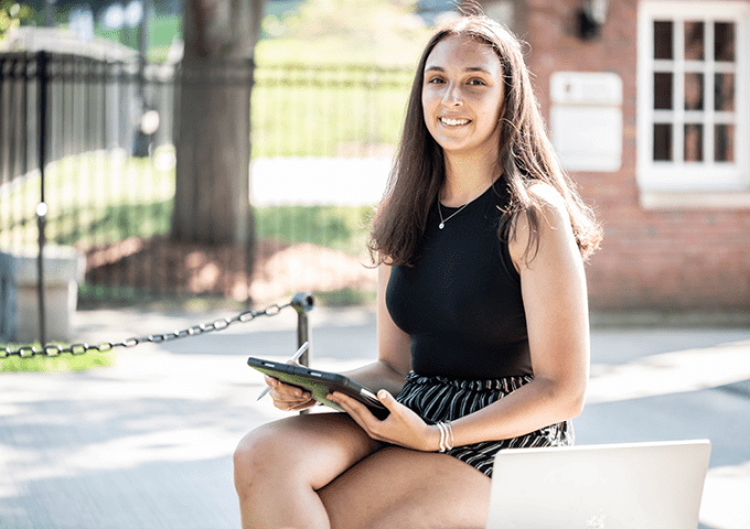 Female civilian student sitting on campus bench with her iPad.