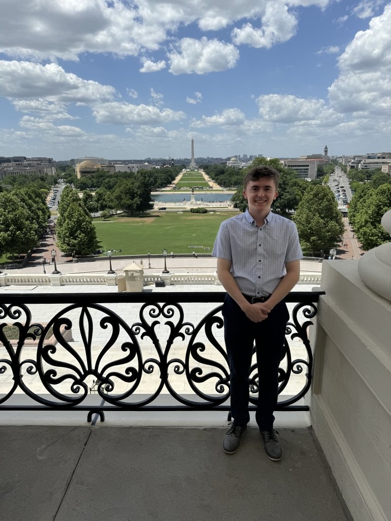 Spencer Rada on the balcony of the Capitol Building with the Washington Monument in the distant background.