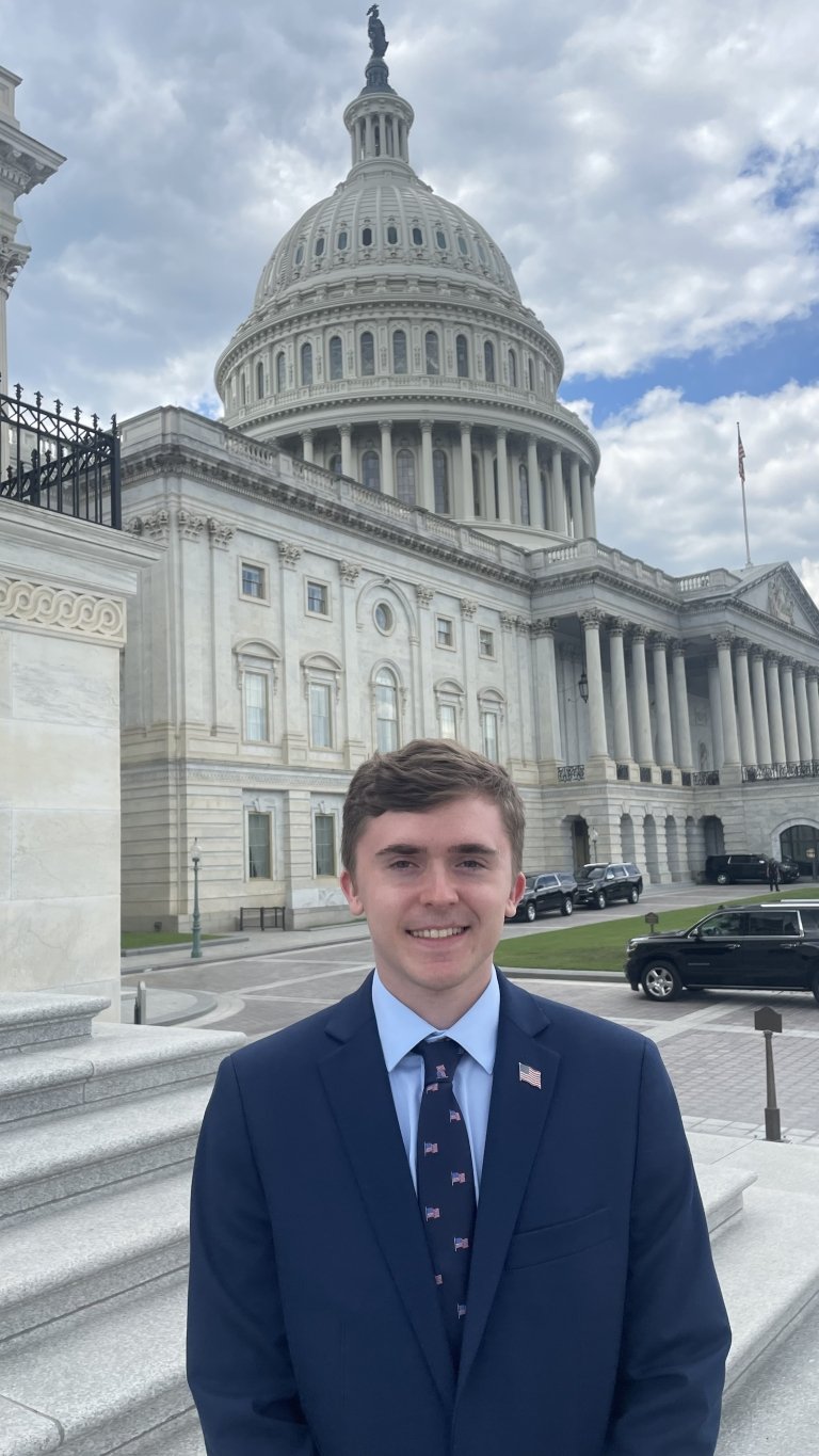 Spencer standing in front of the Capitol Building in a suit and tie.