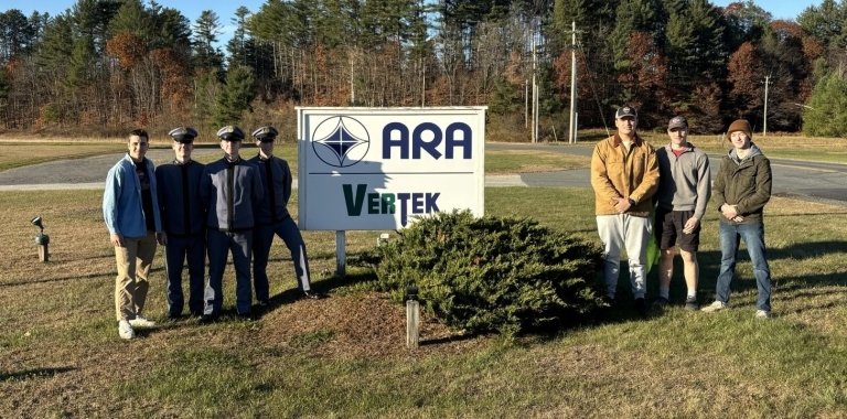 Norwich University students standing in front of the sign for Applied Research Associates in Randolph, VT